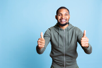 Happy pleased young man giving like sign in front of the camera, posing with positive vibes and...