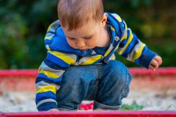 Conceptual image: happy childhood. A little boy builds castles in the sandbox.