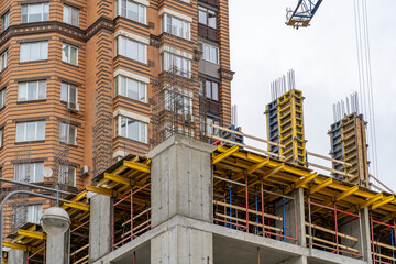 Contrasting modern urban development with completed brick apartment complex standing beside concrete building under active construction, featuring yellow scaffolding and formwork.