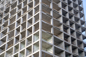 Striking low-angle view of modern multi-story concrete high-rise building under construction, revealing its robust geometric framework, unfinished window openings, and early insulation against clear s