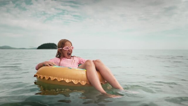 Chid relaxing on inflatable ring alone in open sea, parents monitor safety behind scenes. Calm summer moment with clear water and blue sky, representing peaceful vacation and joyful childhood freedom.