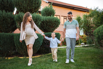 Expecting family enjoys a joyful stroll in green garden