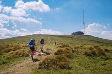 Mother with son trekkers with backbacks using tracking poles walking up to Kralova Hola 1946m mountain with TV transmitter by Slovakian Low Fatras range. Active lifestyle concept image. © Soloviova Liudmyla
