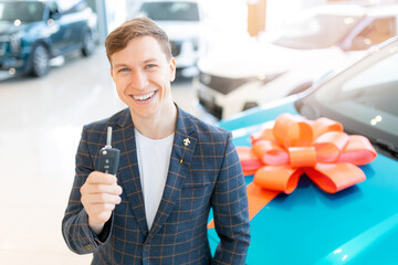 Young caucasian male buying new car at dealership with a gift bow
