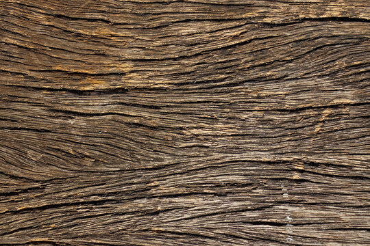 This close-up photograph reveals the rough texture and grains of an old wooden board, showing cracks and the natural dark color of the material.