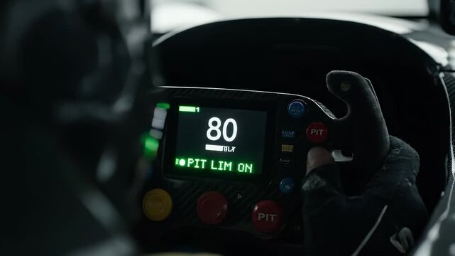 Racing driver in black gloves adjusts controls on high-tech steering wheel, displaying speed and pit limiter status, showcasing intense focus and precision in motorsport environment