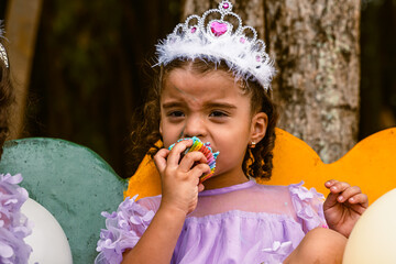 Little girl bites into her cupcake with joy during outdoor birthday celebration. © Daniel Ching