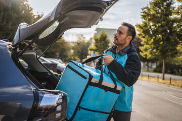 Delivery driver opening car trunk holding thermal bag
