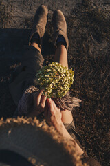 Beautiful young woman is sitting in the meadow with a brunch of hydrangea in her hand. End of summer, girl is happy and enjoying warm sunny day. Author color correction and stylish outfit.