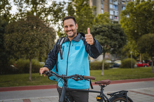 Delivery man with bicycle showing thumb up in urban city park