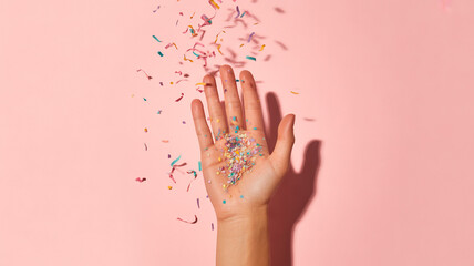 Hand throwing colorful confetti on pink background celebration concept