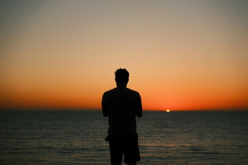 Shadow silhouette of man watching the majestic orange sunset at Sunset Cliffs, Ocean Beach, San Diego, California