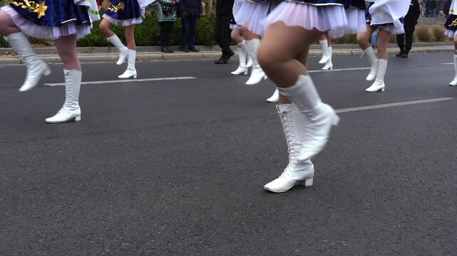 White lace-up majorette boots in motion during parade performance with synchronized marching steps on asphalt street. Drill team choreography, traditional ceremonial footwear, coordinated group. 
