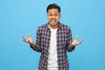 An annoyed and angry man raises his hands and grits his teeth in anger, staring at the camera in annoyance, about to kill someone, standing on a blue background.