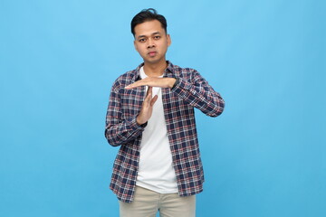 Young Asian man with serious expression, showing time-out or stop gesture, refusing something,...