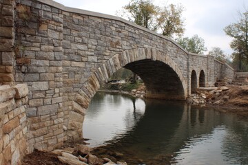 Fototapeta premium Historic Stone Arch Bridge Spanning Serene Waterway Landscape