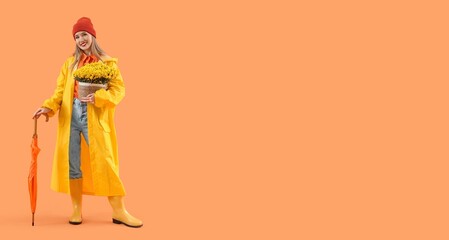 Young woman in raincoat with autumn flowers and umbrella on orange background with space for text