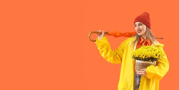 Happy young woman in raincoat with autumn flowers and umbrella on orange background with space for text