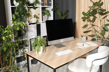 Stylish workplace with modern computer, stationery and floral decor in office. Biophilic interior design