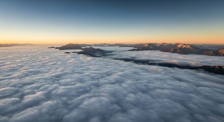Aerial view of mountain peaks emerging from a sea of clouds under a clear blue and orange gradient sky at dawn or dusk.