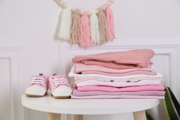 Stack of clean baby clothes and shoes on white table indoors, closeup