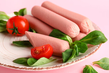 Plate of tasty sausages with basil and tomatoes on pink background