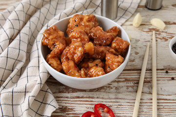 Bowl with tasty sweet and sour chicken on light wooden background, closeup