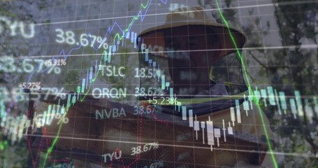 Inspecting beekeeper wearing beekeeping suit holding bee-covered frame in apiary, with stock charts