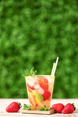 Glass of strawberry lemonade on white wooden table outdoors