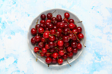 Plate with red sweet cherries on light blue background