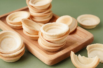 Wooden board with homemade tartlets on green background