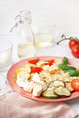 Plate of tasty pasta salad with tomatoes and basil on white background