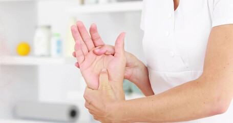 Therapist in uniform pressing forearms kneading client open palm at spa with shelving and towel