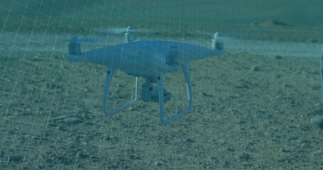 Hovering quadcopter drone capturing aerial footage over barren gravel terrain, grid overlay