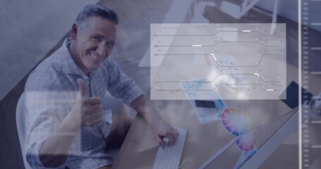 Smiling designer giving thumbs-up in home loft office, with computer monitor and color wheel sheets