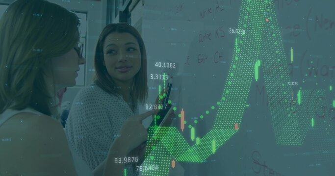 Pointing female colleagues analyzing financial chart overlay on whiteboard, with marker and tablet