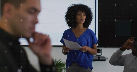 Female wearing blue blouse and pants presenting line chart in meeting room, with screen and docs