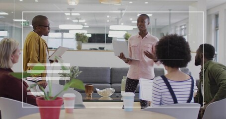 Presenting woman in pink shirt holding laptop addressing team in lounge, with tablet, paper cups