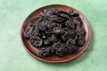Plate with tasty dried plums on green background