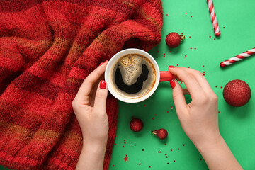 Female hands with red manicure, cup of coffee, knitted scarf and Christmas decor on green background