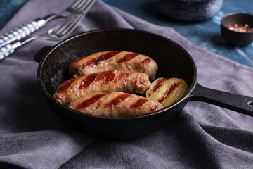 Frying pan with tasty grilled sausages and onion on blue background