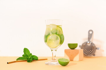 Glass of fresh mojito with straw and cocktail strainer on beige table against white background