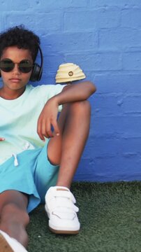 Vertical video: On start, boy in sunglasses is tilting head, adjusting arm on turf to stay relaxed