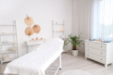 Blurred view of light spa salon with couch, candles and white furniture