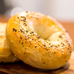 Two bagels, golden brown, topped with poppy seeds and sesame seeds, rest on a wooden board