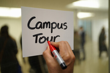 Hand writes campus tour on a note with a red marker inside a building