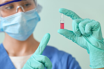 Female doctor pointing at ampoule on green background, closeup