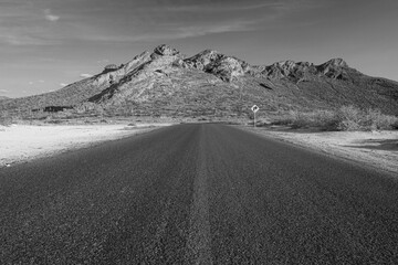 Black and white photograph of a road with a mountain in the background towards El Tecolote beach in...