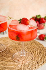 Glass of drink with ice cubes and strawberries on white table against beige wall