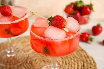 Glasses of drink with ice cubes and strawberries on white table against beige wall